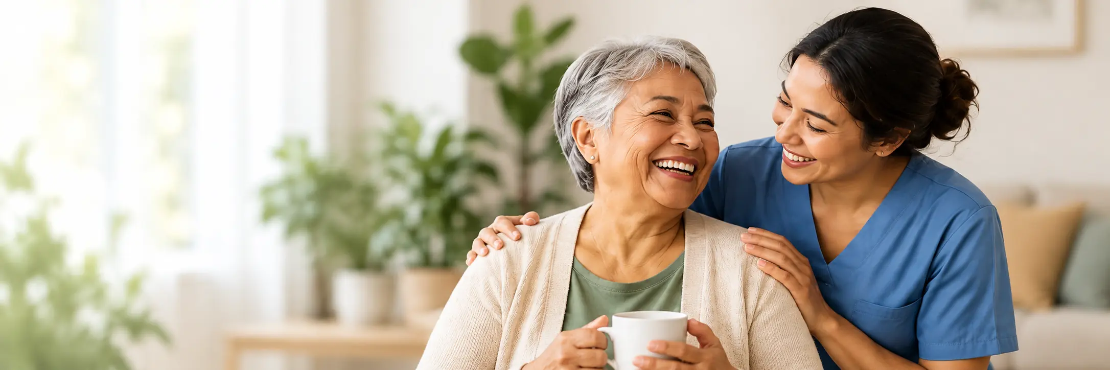 A caregiver and elderly woman laughing together while sharing a warm moment at home